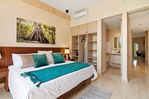 Ein Schlafzimmer mit Bett, Nachttischen, einem Kleiderschrank und einem durchgehenden Türspalte erkennbaren Badezimmer.