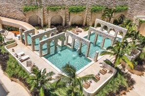 Un área de piscina con arcos de piedra, sillones de descanso y palmeras.
