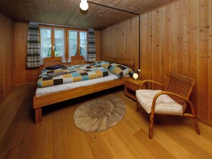 A wooden-paneled room with a bed, a chair, and a nightstand.