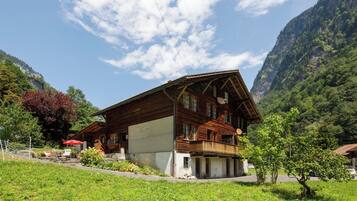 Un chalet en bois doté d’un balcon, entouré d’une végétation luxuriante et de montagnes.