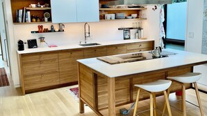 A modern kitchen with wooden cabinetry, a central island, and bar stools. - Wonderful Arboretum 3br custom home w/spectacular outdoor living (Seattle)