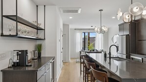 A modern kitchen with a central island, bar stools, a coffee machine, and a built-in wine rack.