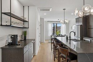 A modern kitchen with a central island, bar stools, a coffee machine, and a built-in wine rack. - Stylish retreat ft. rooftop lounge w/ tub & views! (Nashville)
