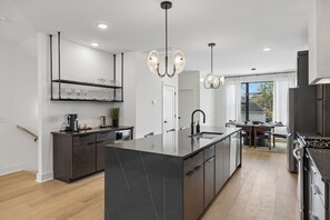 A modern kitchen with a central island, dark cabinetry, and pendant lighting. - Stylish retreat ft. rooftop lounge w/ tub & views! (Nashville)