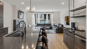 A modern kitchen with a central island, dark cabinetry, and a dining area with chairs.