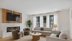 Ein modernes Wohnzimmer mit Flachbildfernseher, Kamin, Sofa, Sesseln und Couchtisch.