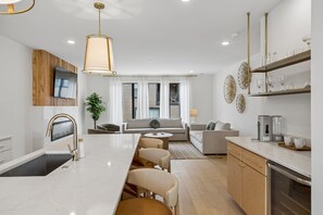 A modern kitchen with a central island, a dining area, and a living space with a sofa and coffee table.