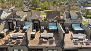 A rooftop with multiple hot tubs and outdoor seating areas, surrounded by residential buildings and a mountainous backdrop. - Upscale home featuring rooftop lounge with hottub! (Nashville)
