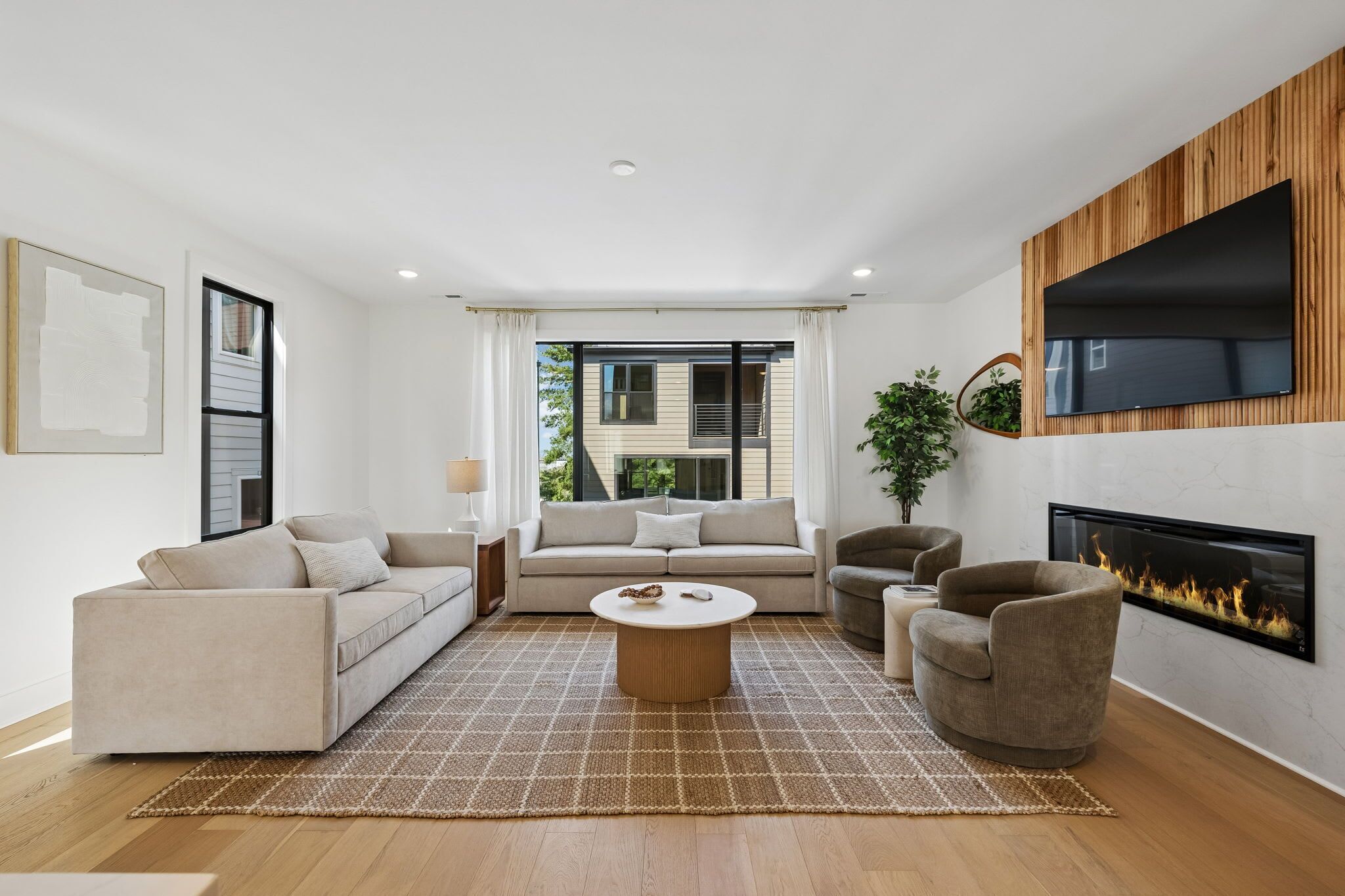 A modern living room with a sofa, armchairs, a coffee table, a fireplace, and a TV mounted on a wooden wall.