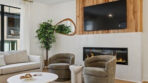 A modern living room with a sofa, two armchairs, a coffee table, a fireplace, a TV mounted on a wooden wall, and a large mirror. - Exclusive townhome ft. rooftop lounge w/ hot tub! (Nashville)