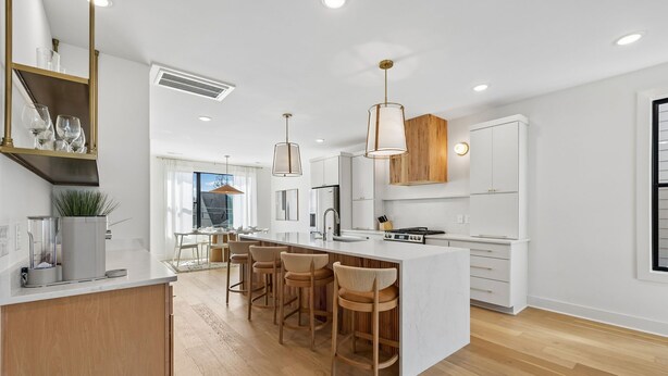 A modern kitchen with a central island, bar stools, pendant lights, and white cabinetry. - Exclusive townhome ft. rooftop lounge w/ hot tub! (Nashville)