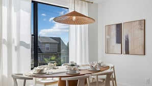 A dining area with a round table, white chairs, a woven pendant light, and artwork on the wall. - Exclusive townhome ft. rooftop lounge w/ hot tub! (Nashville)