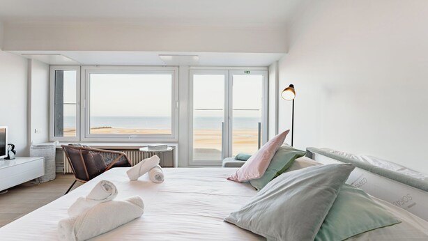 Une chambre d’hôtel avec un lit, des oreillers, une chaise, une lampe, un radiateur et une vue sur la plage.