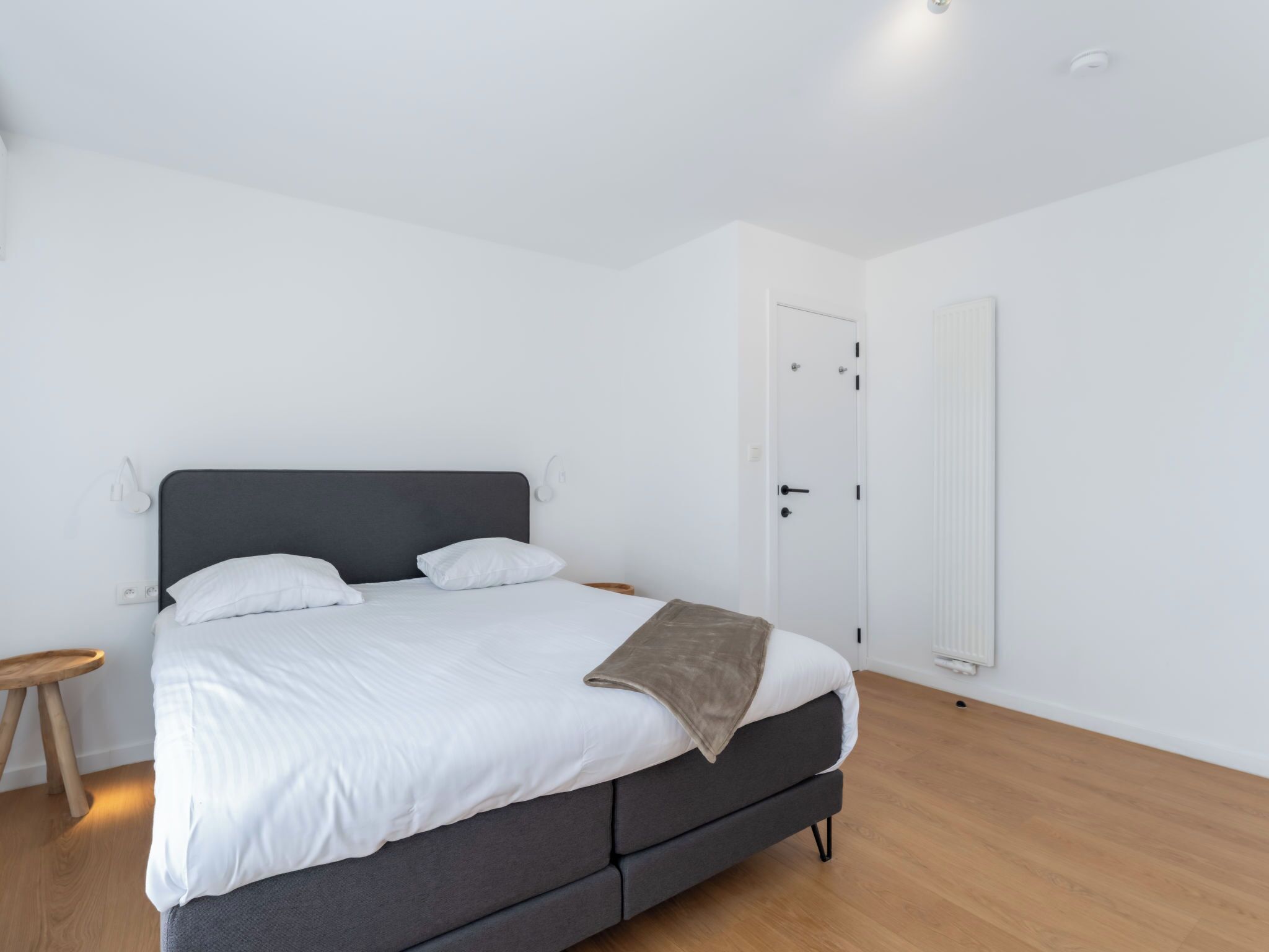 A modern bedroom with a bed, bedside tables, a radiator, and a door.