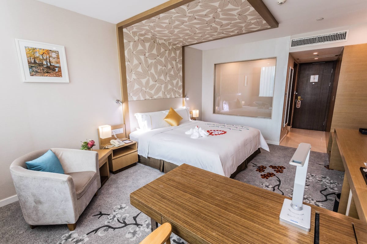 Habitación de hotel con cama, escritorio, silla, mesita de noche, lámpara y un cuadro en la pared.