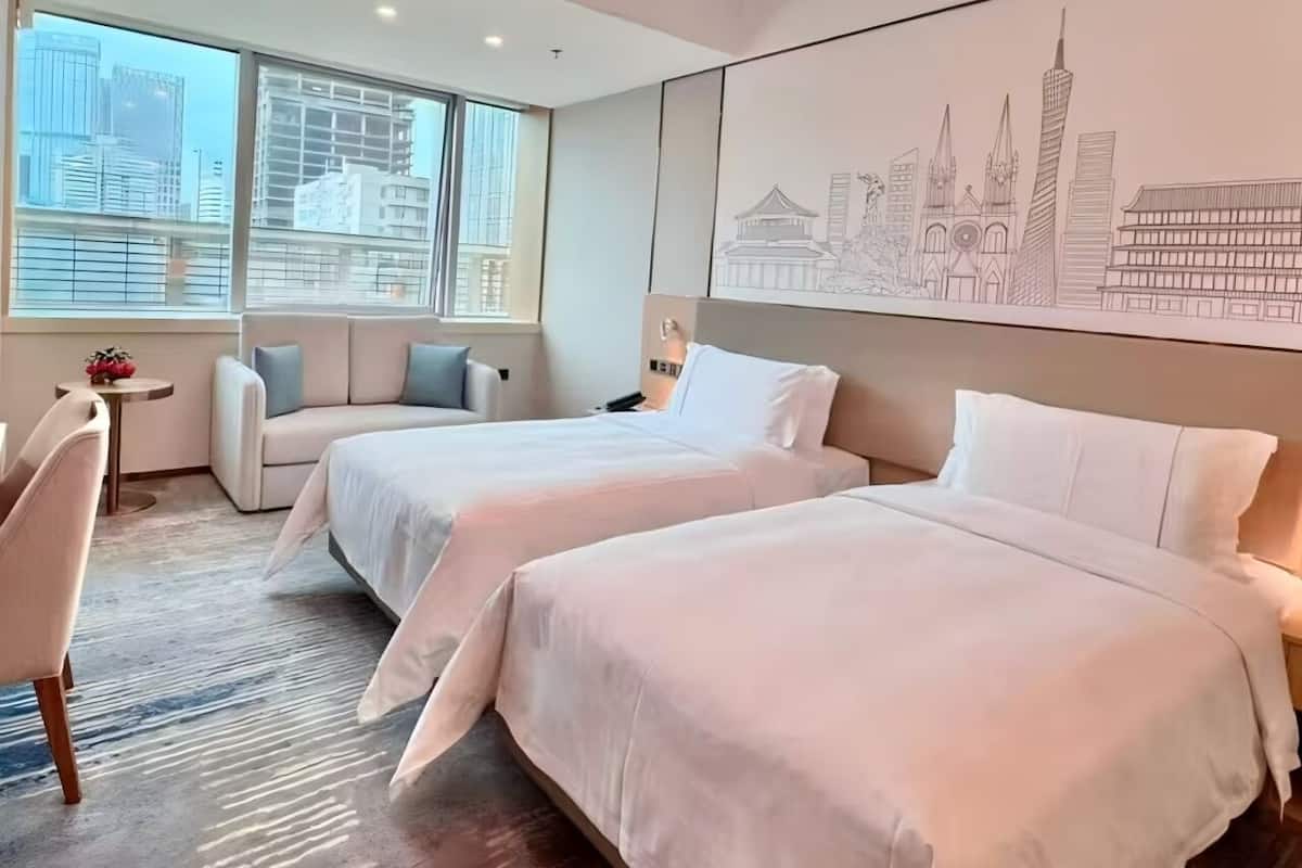 Una habitación de hotel moderna con dos camas, un sofá, un escritorio y un amplio ventanal con vistas a la ciudad.