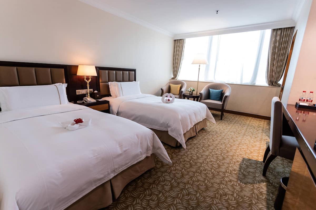 Habitación de hotel con dos camas, un escritorio, una silla, una lámpara y una ventana con cortinas.
