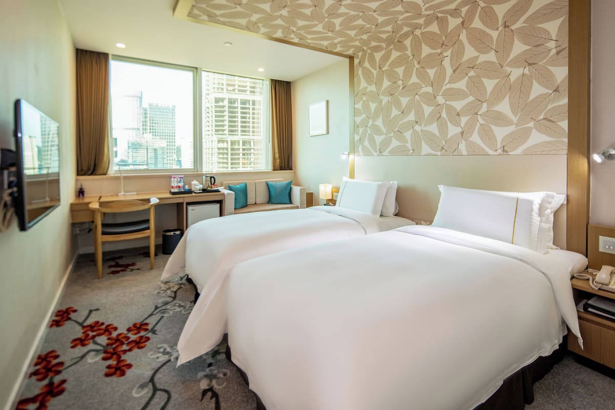 Habitación de hotel con dos camas, un escritorio, una silla, un ventanal con vista a la ciudad y un papel tapiz estampado.