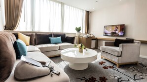 A modern living room with a sofa, armchair, coffee table, and a TV on the wall. - China Mayors Plaza Hotel (Guangzhou)