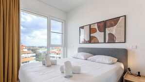 A hotel room with a large bed, a view of buildings through a window, and abstract art on the wall. - Parkville with parking & terrace by Interhome (Blankenberge)