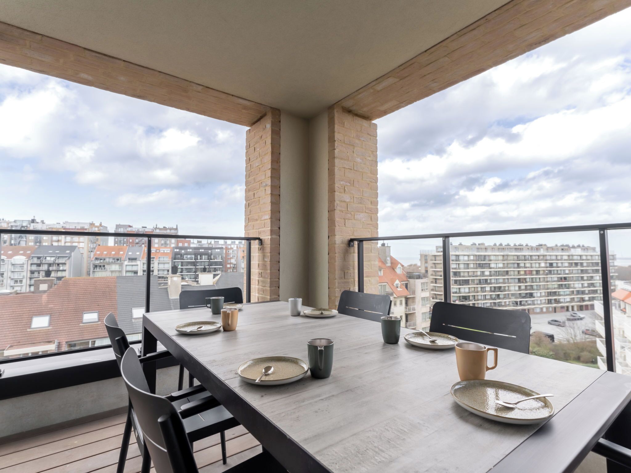 Un balcon avec une table à manger pour quatre personnes, un pilier en briques et une vue sur les immeubles de la ville.