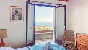 Ein Schlafzimmer mit Bett, Stuhl, Kommode und einem Balkon mit Meerblick.