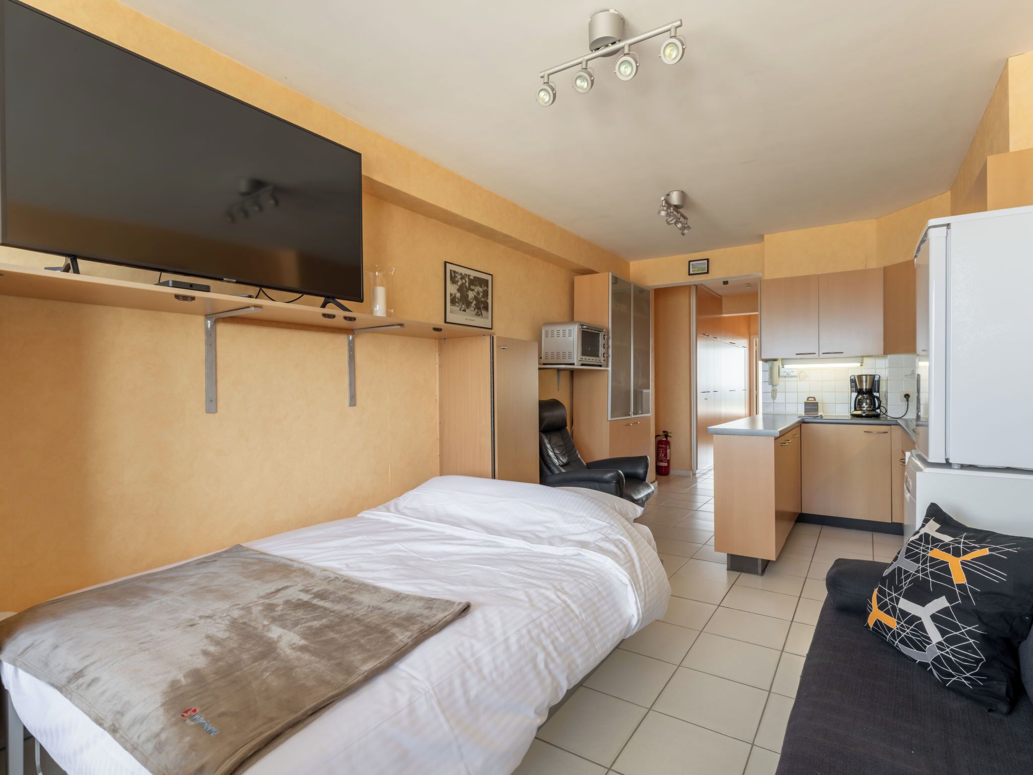 Una habitación de hotel compacta con cama, televisión, kitchenette y zona de estar.