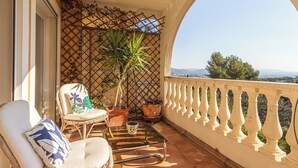 A balcony with wicker furniture, a potted plant, and a view of distant mountains. - Domaine de la Luquette by Interhome (Hyères)