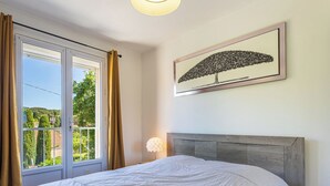 A bedroom with a bed, a window with curtains, a wall-mounted lamp, and a framed picture. - Marius Bondil by Interhome (Six Fours)