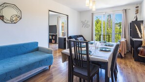 A modern living room with a blue sofa, dining table set for four, and a balcony with a view. - Marius Bondil by Interhome (Six Fours)