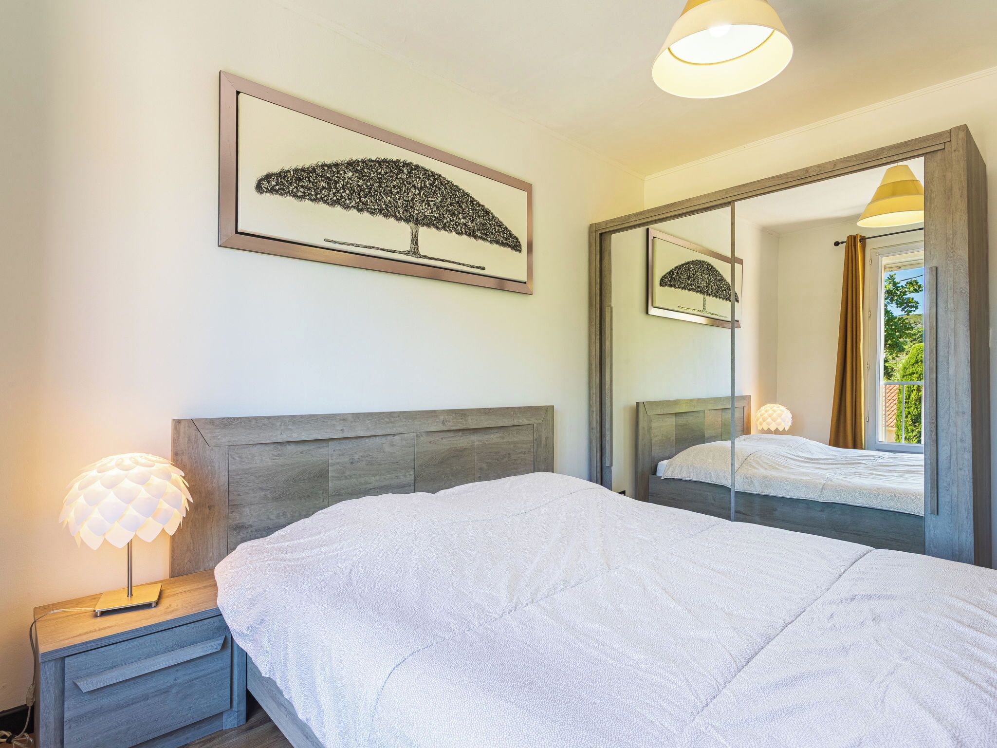 Ein Schlafzimmer mit einem Bett, einem Nachttisch, einer Lampe, einem Spiegel und einem gerahmten Bild an der Wand.