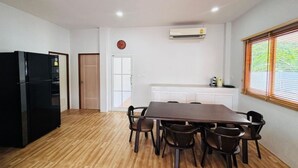 A dining area with a wooden table and chairs, a black refrigerator, a white cabinet, and a window with blinds. - Villa Ao Nang Krabi with a free car (Krabi)
