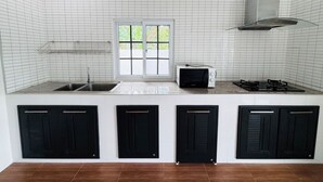 A kitchen with white tiled walls, a window, a white microwave, a gas stove, and black cabinets. - Villa Ao Nang Krabi with a free car (Krabi)