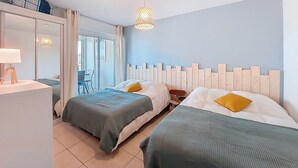 Habitación de hotel con dos camas, un escritorio con lámpara, un armario y un ventanal corredero que da a un balcón.