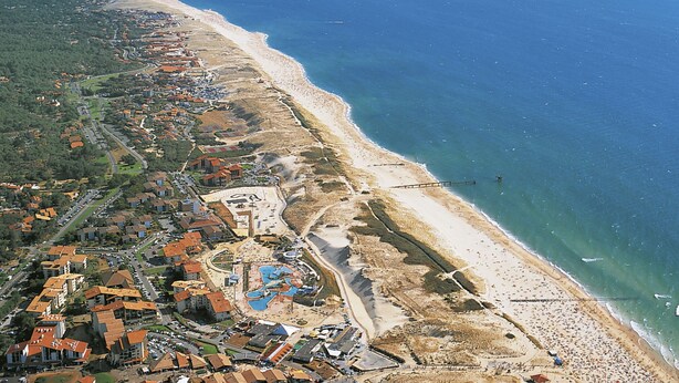 Vista aérea de una zona costera con playa, edificios residenciales y un puerto deportivo.