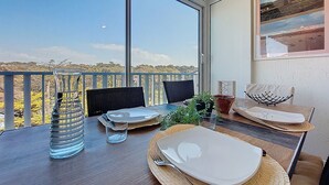 Un comedor con una mesa dispuesta para dos, un ventanal con vistas y una obra de arte enmarcada en la pared.