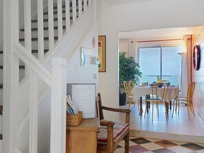 Eine Treppe führt zu einem Essbereich mit Blick auf das Meer, eine Tafel mit einer Notiz und eine Pflanze am Fenster.