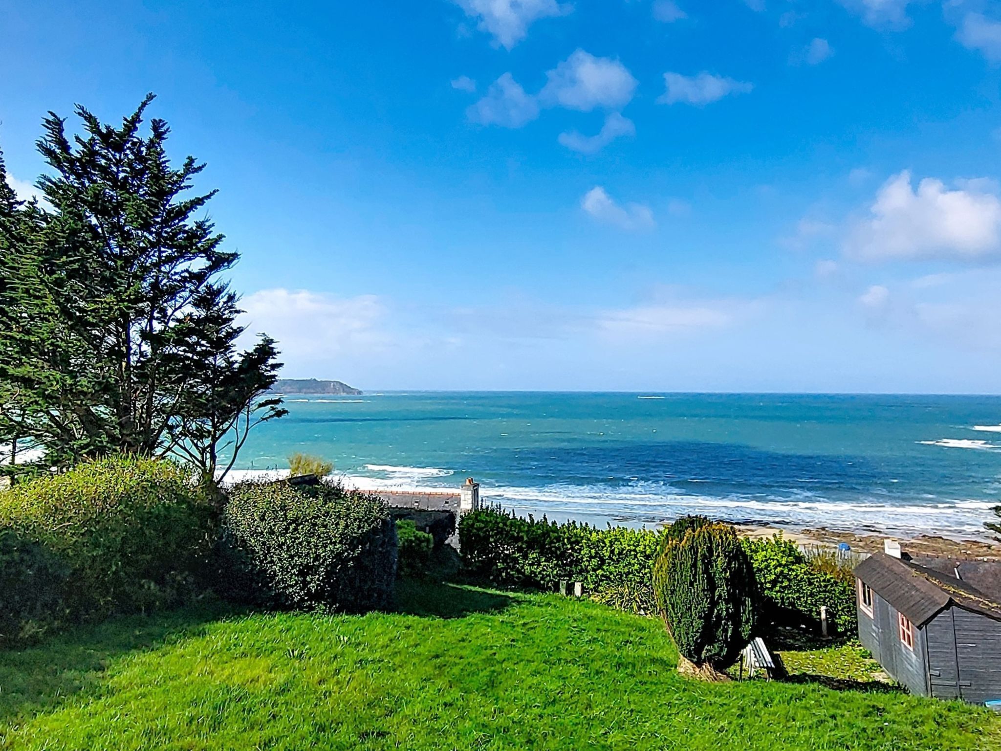 A coastal landscape with a grassy area, a small building, and the ocean in the background.