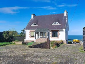 Ein zweistöckiges Haus mit einer Steinfassade, einem dunklen Dach und Blick auf das Meer.