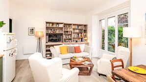 Een woonkamer met een bank, stoelen, een salontafel, een boekenkast en een eettafel.