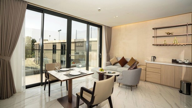 A modern living room with a dining area, a sofa, and a kitchen area with a countertop and shelves. - The Five Hotel & Resort Evara - 24 Hours stay (Hanoi)