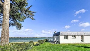 Una casa costera con césped, un árbol y vistas al mar.