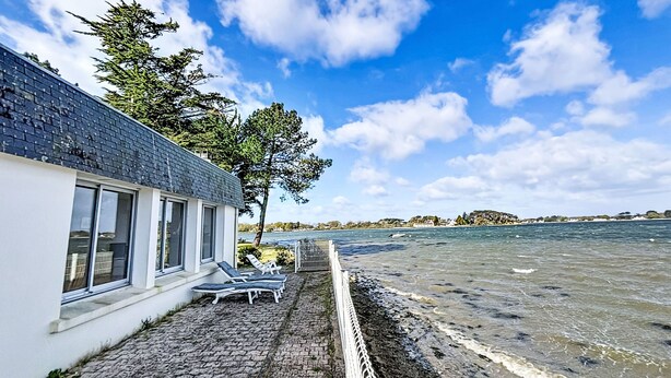 Un edificio costero con un patio empedrado, sillas de lounge y vista al mar.