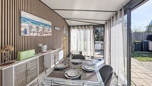 Un'area pranzo all'aperto coperta con un tavolo apparecchiato per quattro persone, un mobiletto in legno con un quadro e vista sul giardino.