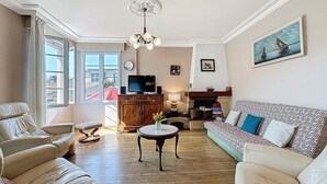 Uma sala de estar com sofá, poltronas, televisão, lareira e um quadro na parede.