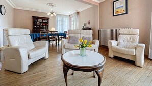 Uma sala de estar ampla com piso de madeira, uma mesa de centro redonda e dois sofás de couro branco.