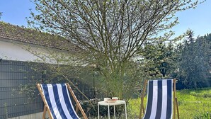 Dos sillas de playa a rayas sobre una terraza de madera con una mesita y una planta en maceta.