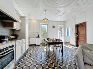 A kitchen with a tiled floor, a dining area with a table and chairs, and a wooden door. - L'Ecluse by Interhome (Les Moutiers-en-Retz)