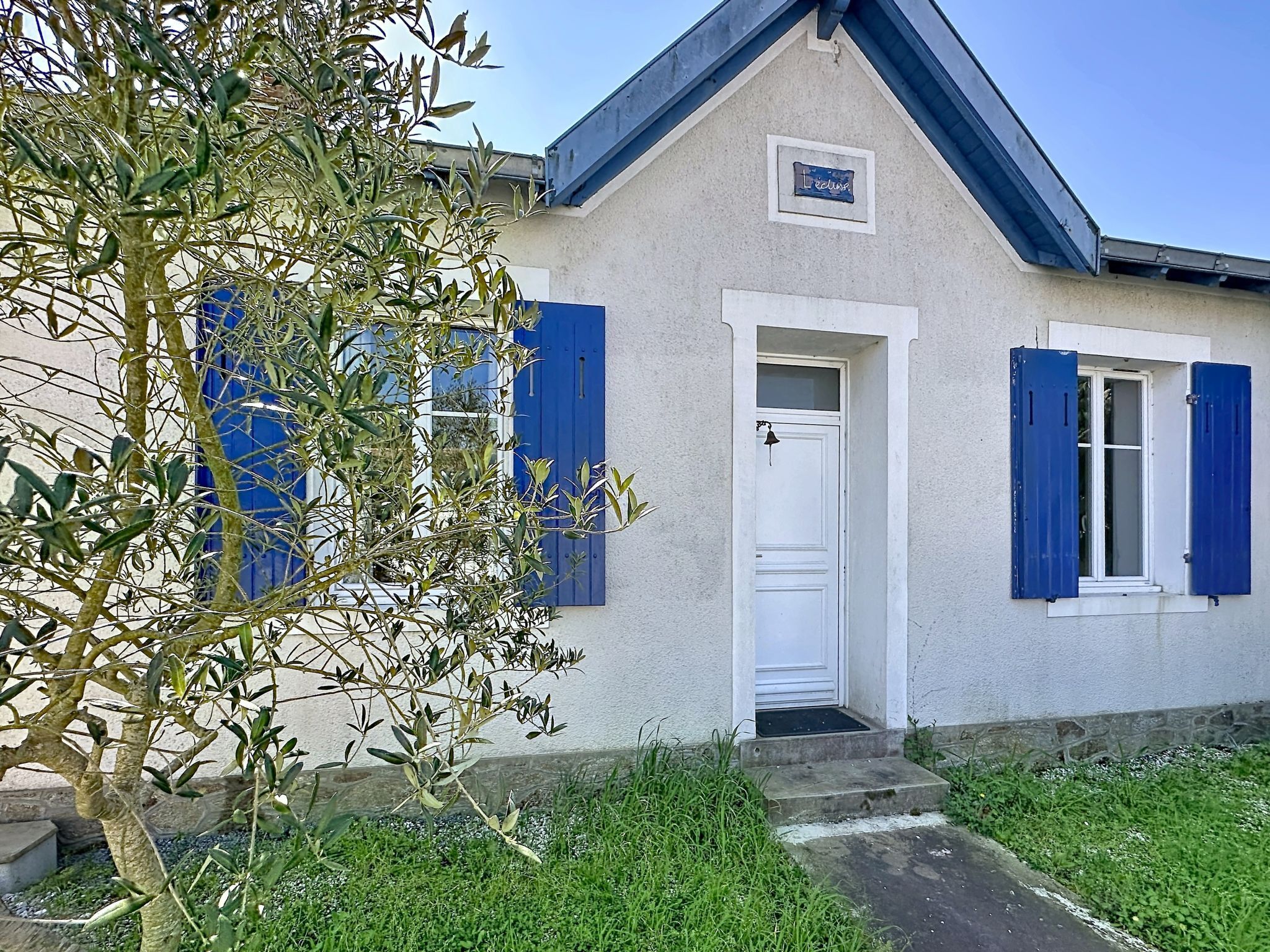 A house with a white door, blue shutters, and a small sign above the door.