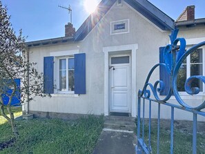 Uma casa com porta branca, venezianas azuis e um pequeno jardim.